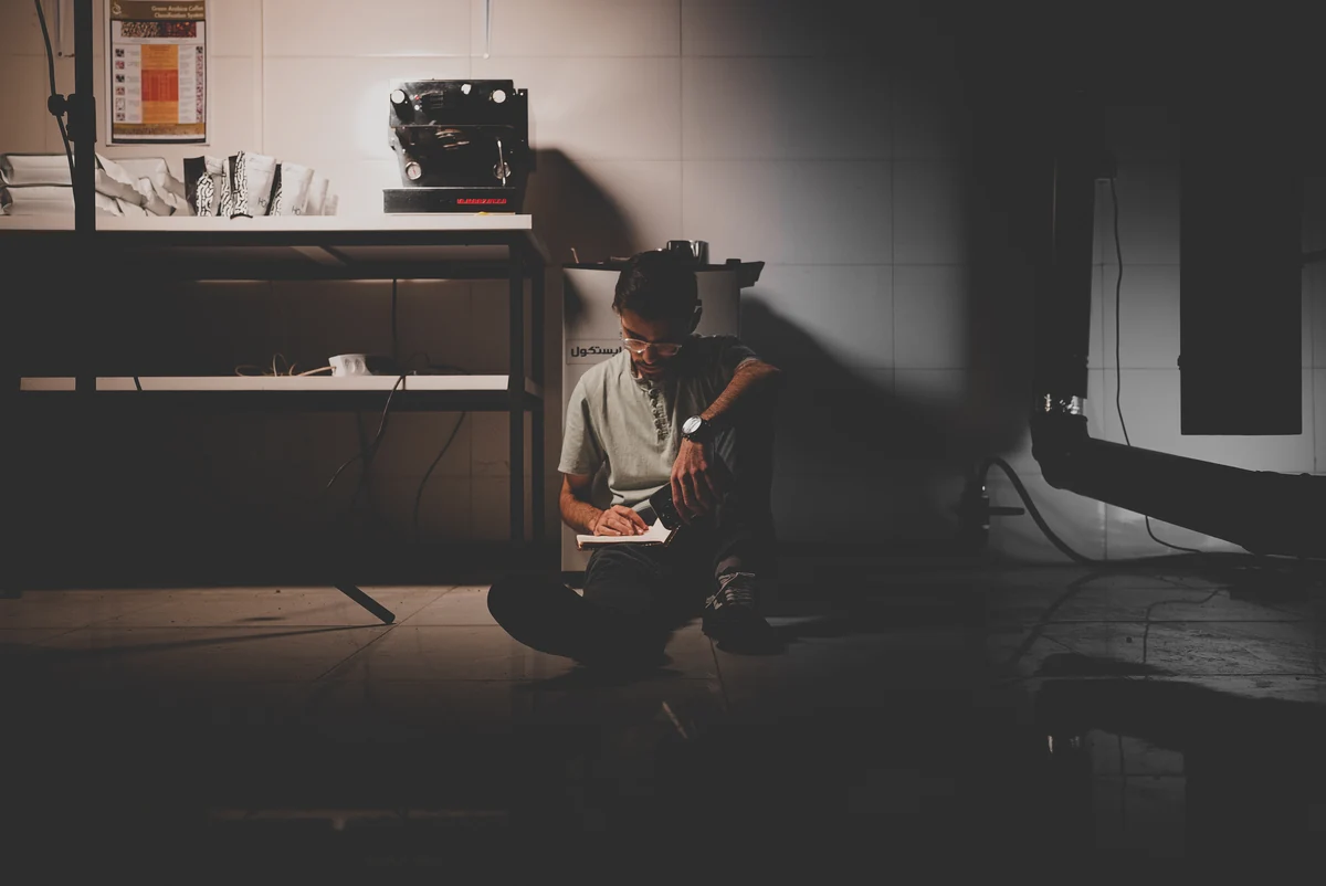 A man writing in a notebook on the floor of a coffee studio