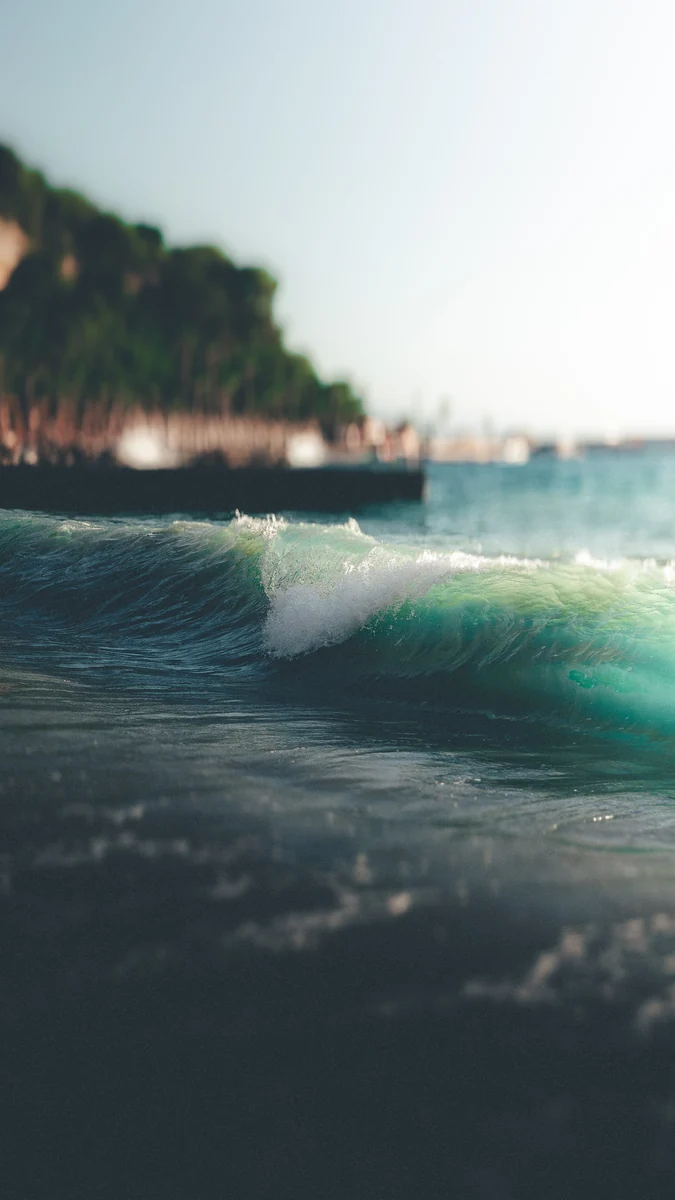 A small turquoise wave breaking near the waterfront
