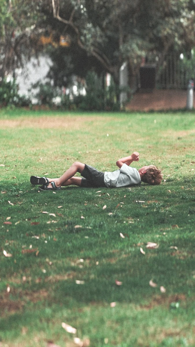 A child playing on a lawn beneath leafy trees