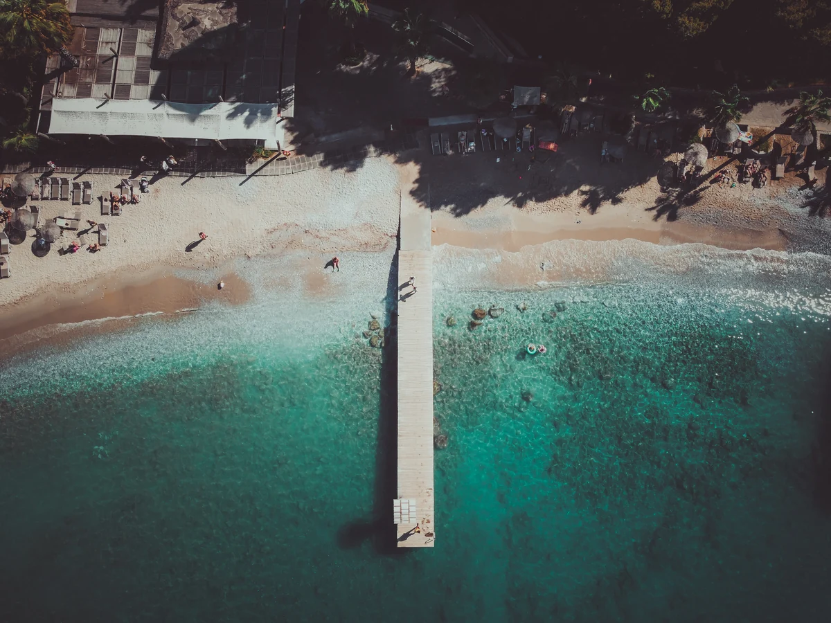 An overhead view of a long pier extending into turquoise water